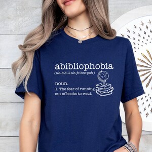 May include: A navy blue t-shirt with white text that reads "abibliophobia (uh-bib-li-uh-fo-bee-yuh) noun. 1. The fear of running out of books to read."