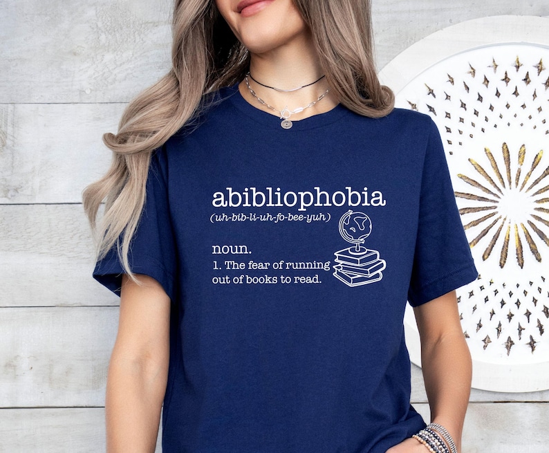 May include: A navy blue t-shirt with white text that reads "abibliophobia (uh-bib-li-uh-fo-bee-yuh) noun. 1. The fear of running out of books to read."