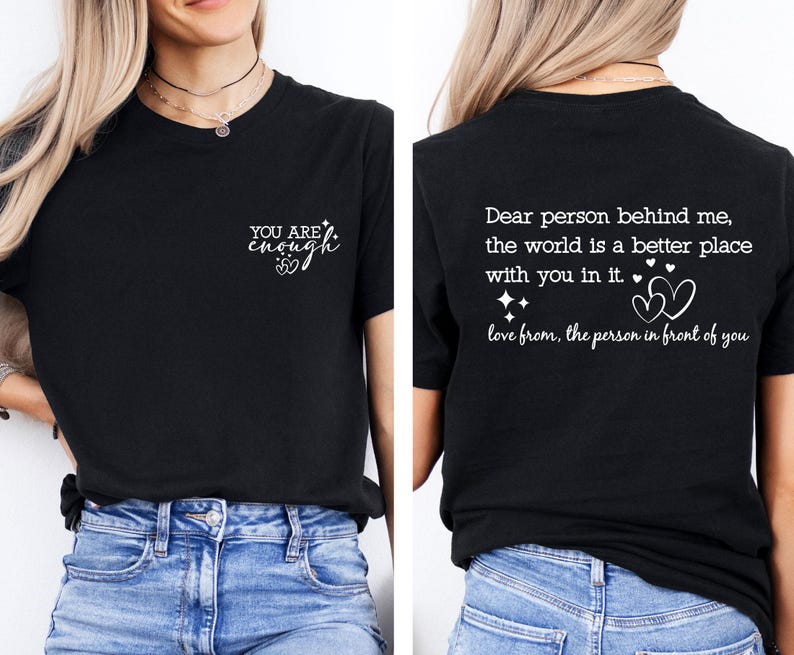May include: Two black t-shirts with white text. The front shirt says "YOU ARE enough" with a small heart symbol. The back shirt says "Dear person behind me, the world is a better place with you in it. love from, the person in front of you" with two heart symbols.
