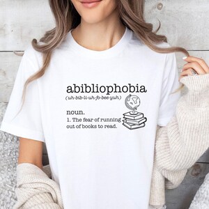 May include: White t-shirt with the text "abibliophobia (uh-bib-li-uh-fo-bee-yuh) noun. 1. The fear of running out of books to read." and a drawing of a globe on top of a stack of books.