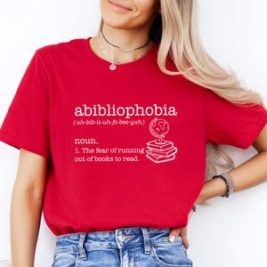May include: Red t-shirt with white text that reads "abibliophobia (uh-bib-li-uh-fo-bee-yuh) noun. 1. The fear of running out of books to read."