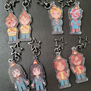 May include: Eight colorful cartoon character keychains with party hats. Each keychain features a different character with a unique design and is attached to a silver star-shaped charm.