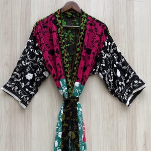 May include: A long-sleeved kimono robe featuring a patchwork design of black, magenta, and teal fabric panels. The garment is decorated with intricate white and green floral embroidery patterns throughout, including a prominent vine motif along the front.