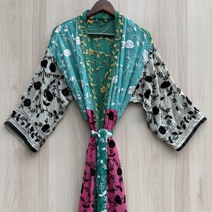 Puede incluir: Una bata de manga larga con un diseño de patchwork en secciones de color verde azulado, rosa y blanco. La prenda está decorada con bordados florales negros en toda su superficie, incluyendo detalles florales blancos en la parte superior.