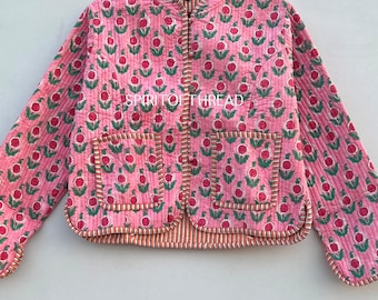 May include: A pink quilted jacket with a floral print and two front pockets. The jacket has a mandarin collar and a button closure. The text "SPIRIT OF THREAD" is printed on the front of the jacket.