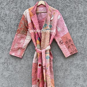 Puede incluir: Bata de patchwork en tonos rosa, melocotón y crema, con detalles florales bordados. La bata presenta un cuello chal, mangas largas y un cinturón a juego. El texto "Spiritofthread" es visible en la bata.