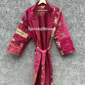 Op de afbeelding: Een magenta patchwork kamerjas met lange mouwen en ingewikkelde kantha-stiksels over het hele oppervlak. Het kledingstuk is voorzien van een ceintuur, een reverskraag en diverse bloem- en geometrische patronen in goud- en meerkleurig garen. De tekst Spiritofthread is zichtbaar.