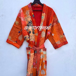 May include: A patchwork robe in shades of orange and red featuring various floral and geometric patterns, long sleeves, a tie belt, and two front pockets. The text SPIRITOFTHREAD is printed in white across the chest area of the garment.