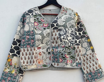 May include: A patchwork quilted jacket with a V-neck and button closure. The jacket is made of cotton fabric and features a variety of floral and geometric patterns in shades of blue, green, white, and black. The text "SPIRIT OF THREAD" is visible on the front of the jacket.