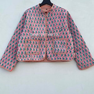 May include: A pink quilted jacket with a floral print and a mandarin collar. The jacket has two pockets and a button closure. The jacket is lined with a contrasting orange fabric.