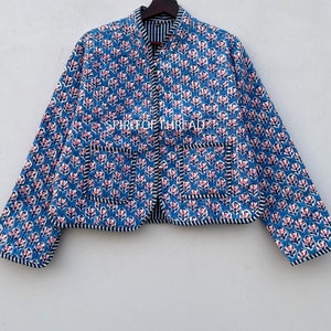 Puede incluir: Chaqueta acolchada azul con un estampado floral en rosa y blanco. La chaqueta tiene cuello mandarín, dos bolsillos y ribete a rayas blancas y negras. La chaqueta mide aproximadamente 63,5 cm de largo.