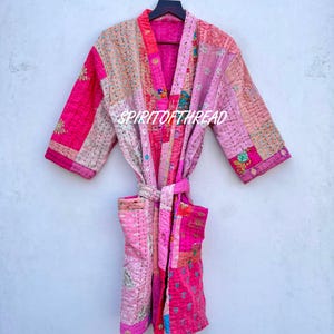 May include: A patchwork robe in shades of pink, fuchsia, and peach, with a matching belt. The robe features a variety of fabric patterns and textures, including floral and geometric designs. The text "SPIRITOFTHREAD" is visible on the robe.