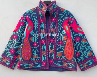 May include: A blue embroidered jacket with a high collar and a floral pattern featuring peacocks, flowers, and leaves in shades of pink, orange, and turquoise. The text "SPIRIT OF THREAD" is embroidered on the front of the jacket.