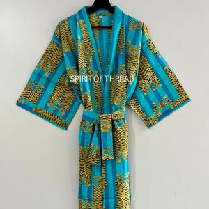 Könnte beinhalten: Türkis-goldener Robe mit Tigerdruck und Streifenmuster. Die Robe hat lange Ärmel und einen passenden Gürtel. Der Text "SPIRITOFTHREAD" ist auf der Robe zu sehen.