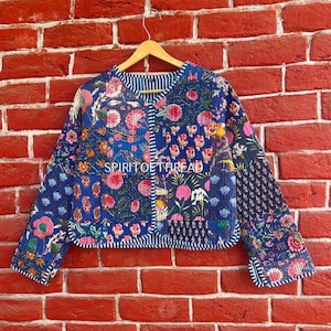 May include: A blue and pink floral patterned quilted jacket with a white stripe down the front. The jacket has a round neckline and long sleeves. The text "SPIRITOETHREAD" is visible on the front of the jacket.