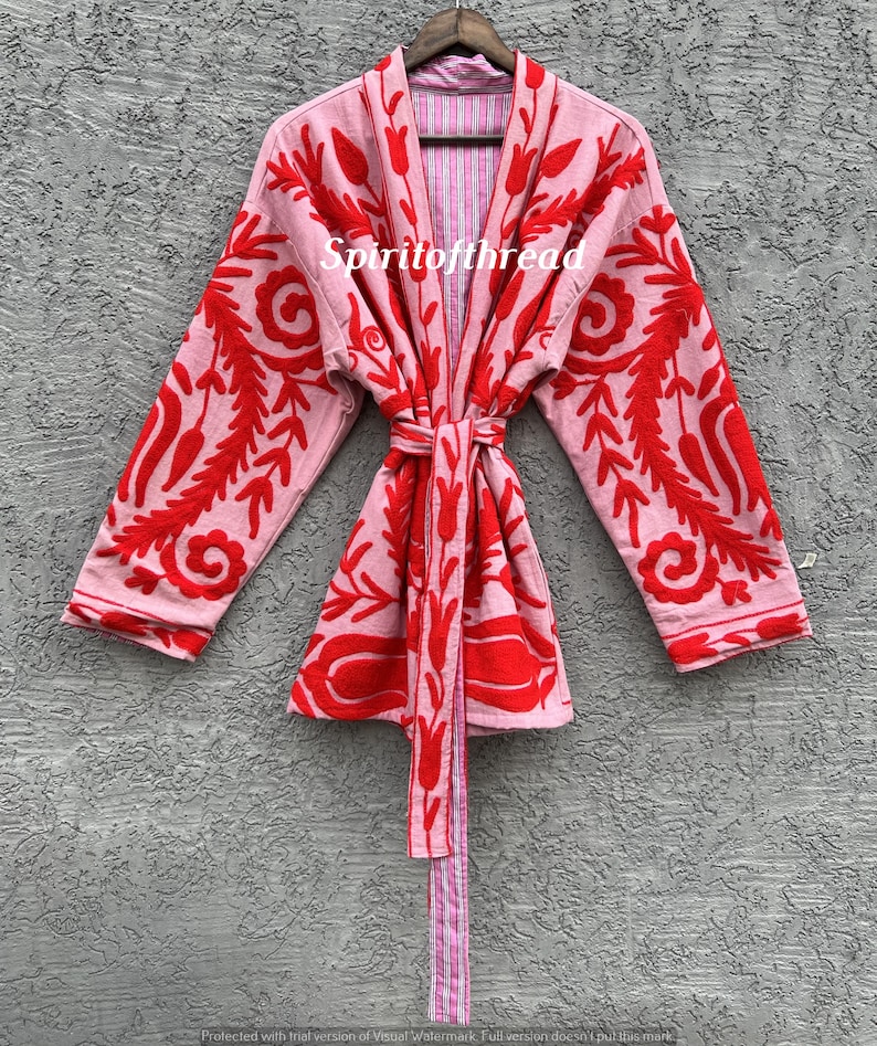 May include: A light pink robe with red floral embroidery and a matching tie. The robe is open, revealing a striped lining. The text "Spiritofthread" is visible on the robe.