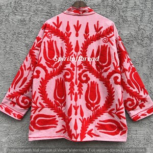 May include: A light pink jacket with red floral embroidery. The jacket features a collared neckline and three-quarter sleeves. The text "Spiritofthread" is visible on the jacket. The embroidery design includes stylized flowers and leaves.