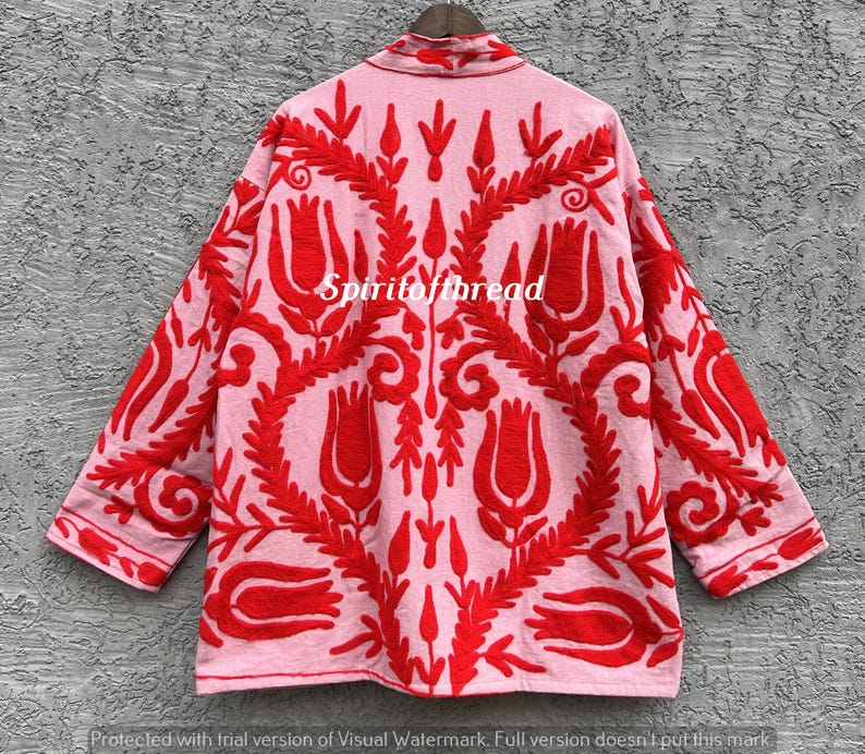 May include: A light pink jacket with red floral embroidery. The jacket features a collared neckline and three-quarter sleeves. The text "Spiritofthread" is visible on the jacket. The embroidery design includes stylized flowers and leaves.