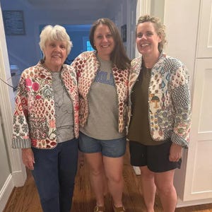 May include: Three people wearing colorful, quilted jackets with floral and geometric patterns. The jackets have a mix of red, pink, blue, and white designs. The jackets are paired with casual outfits, including jeans, shorts, and a t-shirt.