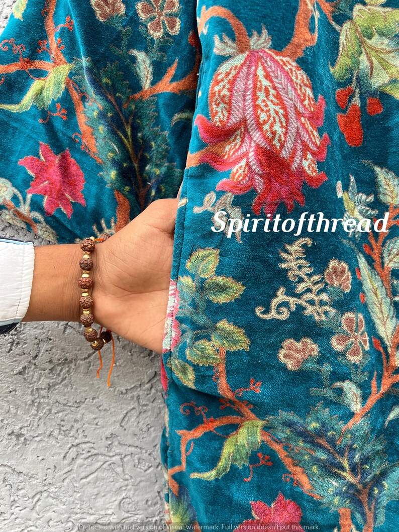 Pode incluir: Casaco de veludo azul-petr&oacute;leo com um padr&atilde;o floral em tons de vermelho, laranja e verde. O casaco tem um bolso e est&aacute; parcialmente aberto, revelando uma manga de camisa branca. O texto "Spiritofthread" &eacute; vis&iacute;vel.