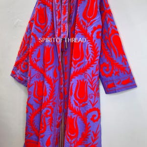 May include: A long, open-front coat in a vibrant purple hue, adorned with intricate red floral embroidery. The coat features a bold design with the text "SPIRITOFTHREAD" visible. This statement piece is a striking addition to any wardrobe.