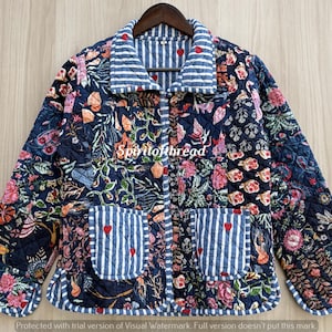 May include: A quilted jacket featuring a dark blue base with a multi-colored floral and botanical print. The garment includes a blue and white striped collar, cuffs, and two front pockets, each accented with small red heart embroidery.