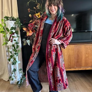 May include: A long, open-front robe in shades of red and burgundy, with vertical stripes and tiger patterns. The robe has a striped lining and is made of a soft, velvety material. A stylish garment for layering.