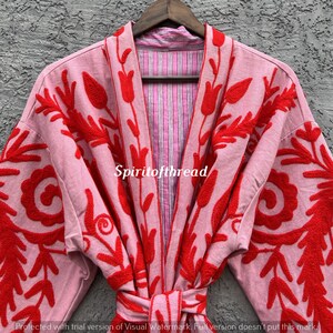May include: A light pink robe with red floral embroidery. The robe has a striped pink and white lining and a matching belt. The text "Spiritofthread" is visible on the robe.