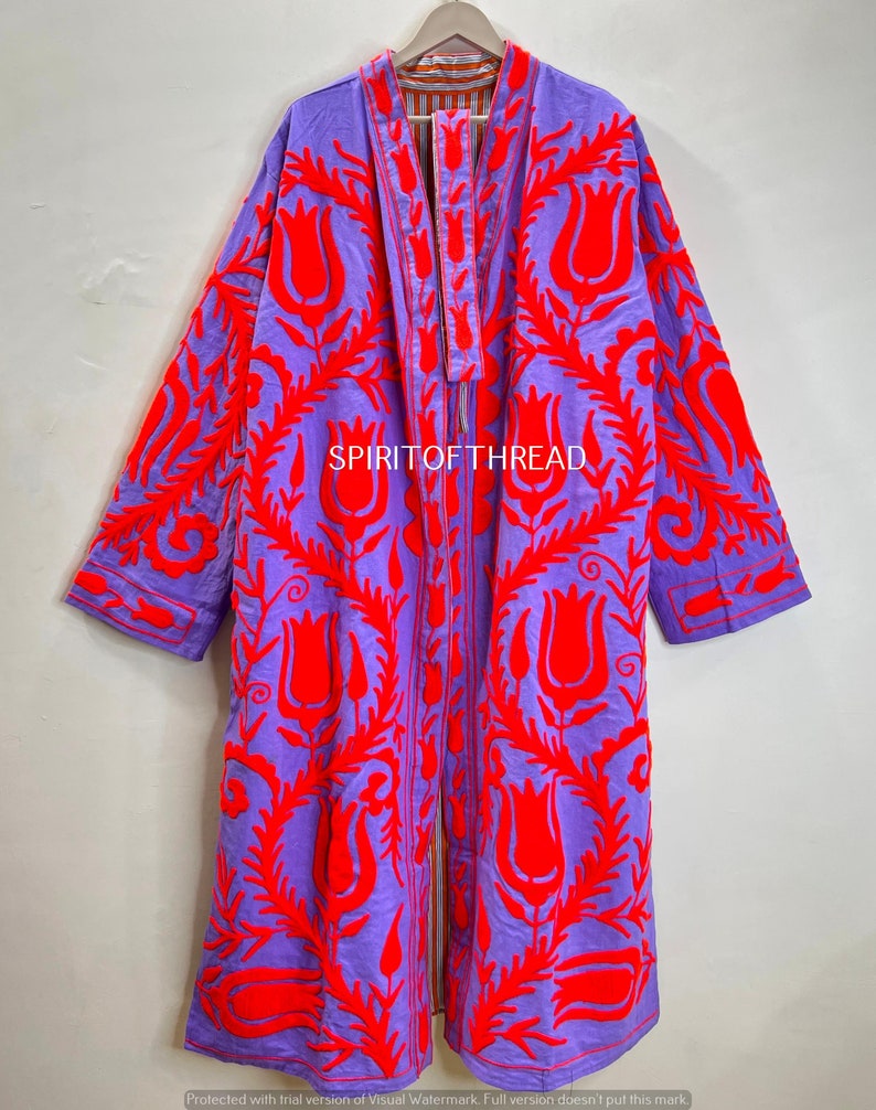 May include: A long, open-front robe in a vibrant purple hue, adorned with bold red floral embroidery. The robe features long sleeves and a detailed pattern, with the text "SPIRITOFTHREAD" visible. The garment is displayed on a wooden hanger.