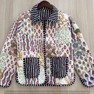 May include: A quilted jacket featuring a patchwork design of various floral and botanical prints in shades of pink, green, blue, and yellow. It has a black and white striped collar, cuffs, and two front pockets with small red heart accents.