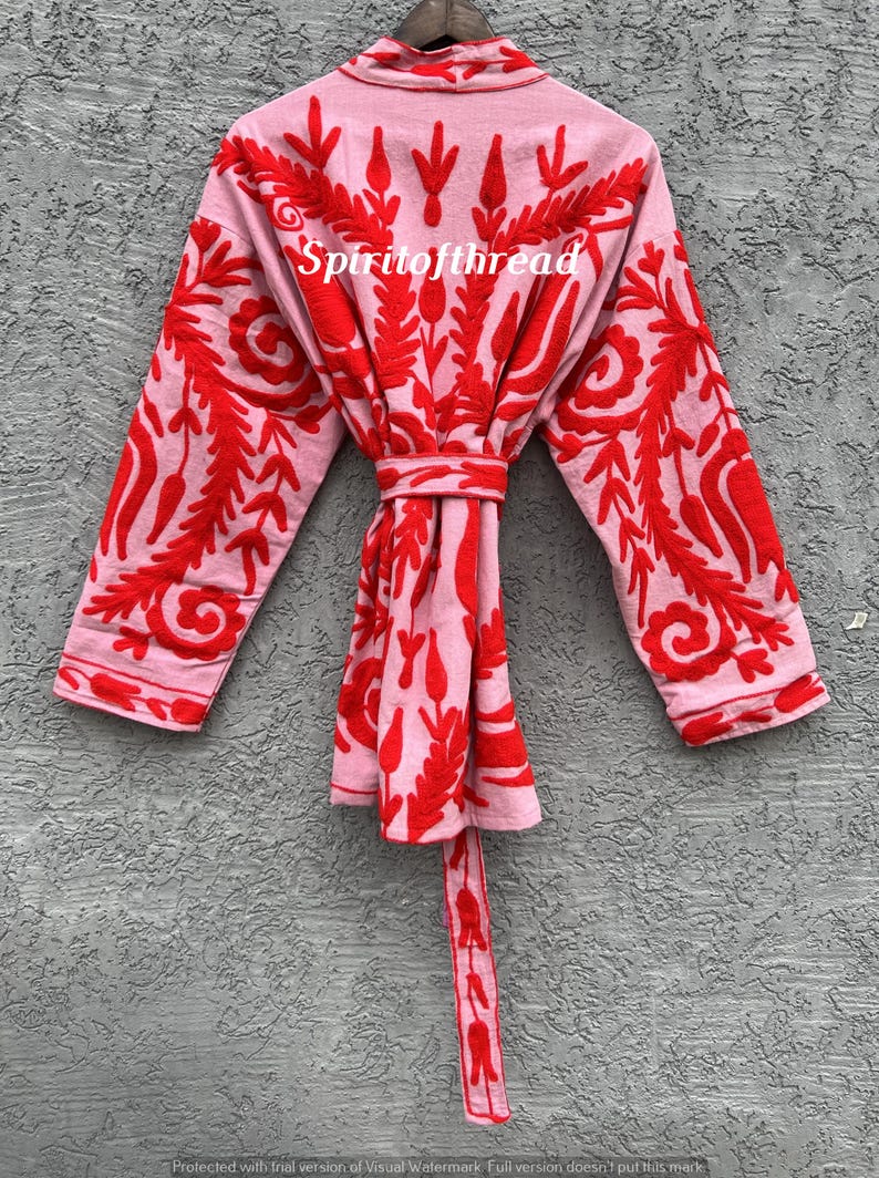 May include: A light pink kimono-style robe with intricate red embroidered floral patterns. The robe has long sleeves and a matching belt. The text "Spiritofthread" is visible on the front of the robe.