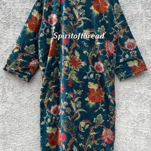 Pode incluir: Um roup&atilde;o com estampa floral azul-petr&oacute;leo com detalhes em vermelho e verde. O roup&atilde;o apresenta um design longo e fluido com uma estampa bot&acirc;nica. O texto "Spiritofthread" &eacute; vis&iacute;vel no roup&atilde;o. O roup&atilde;o &eacute; feito de um material macio e aveludado.