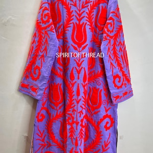 May include: A long, purple tunic with vibrant red floral embroidery. The tunic features a high collar, long sleeves, and side slits. The text "SPIRITOFTHREAD" is visible on the garment. This embroidered tunic is a unique piece of clothing.