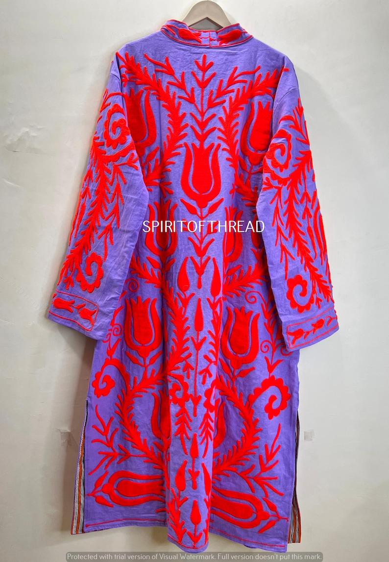 May include: A long, purple tunic with vibrant red floral embroidery. The tunic features a high collar, long sleeves, and side slits. The text "SPIRITOFTHREAD" is visible on the garment. This embroidered tunic is a unique piece of clothing.
