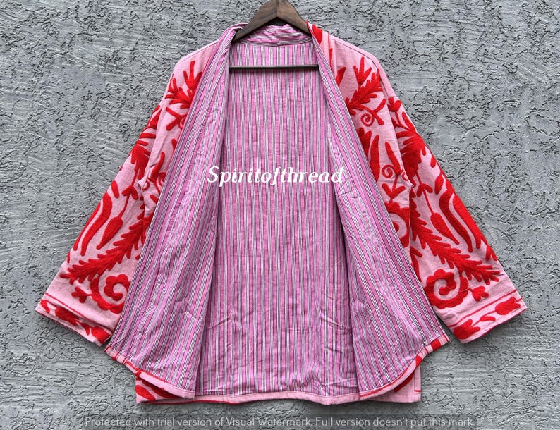 May include: A pink open-front jacket with red floral embroidery on the sleeves and collar. The inside lining features a pink and white striped pattern. The text "Spiritofthread" is visible on the jacket.