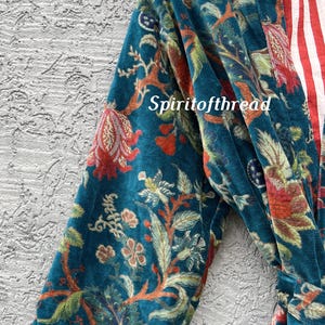 Pode incluir: Um roup&atilde;o de veludo azul-petr&oacute;leo com um padr&atilde;o floral em vermelho, laranja e verde. O forro interior do roup&atilde;o apresenta riscas vermelhas e brancas. O texto "Spiritofthread" &eacute; vis&iacute;vel.