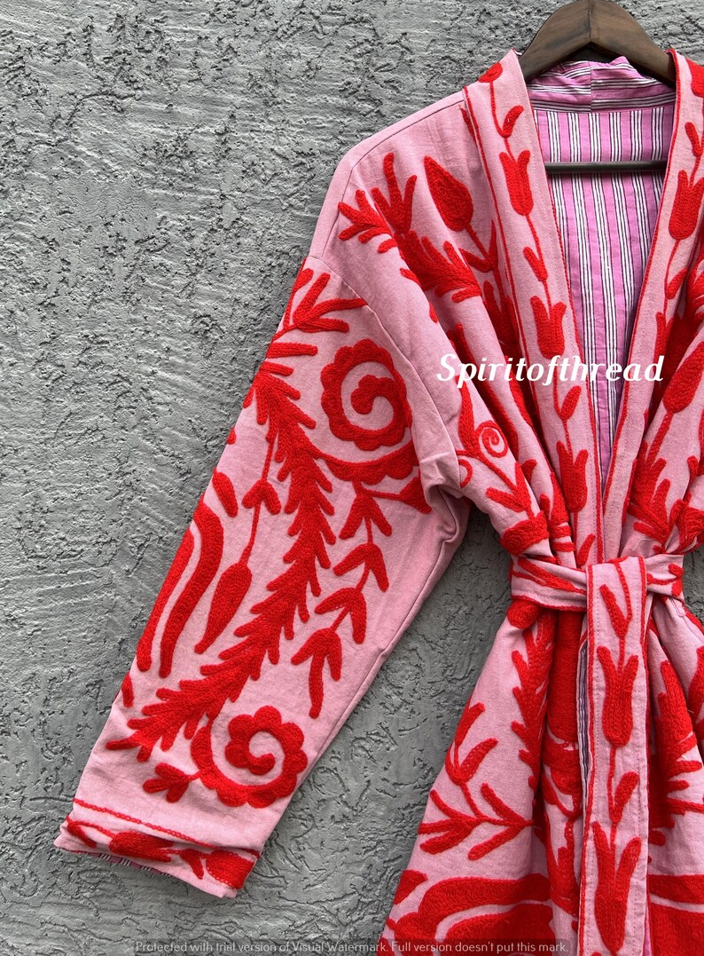 May include: A light pink robe with red floral embroidery. The robe features long sleeves and a tie belt. The interior lining is striped pink and white. The text "Spiritofthread" is visible on the robe.