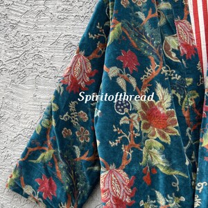 Pode incluir: Um quimono de veludo azul-petr&oacute;leo com um padr&atilde;o floral em vermelho, verde e castanho. O interior do quimono apresenta riscas vermelhas e brancas. O texto "Spiritofthread" &eacute; vis&iacute;vel na frente da pe&ccedil;a.