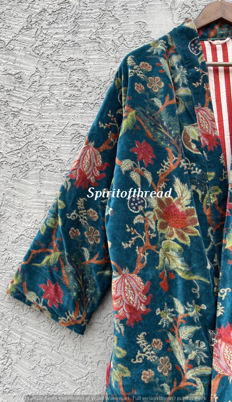 Pode incluir: Um quimono de veludo azul-petr&oacute;leo com um padr&atilde;o floral em vermelho, verde e castanho. O interior do quimono apresenta riscas vermelhas e brancas. O texto "Spiritofthread" &eacute; vis&iacute;vel na frente da pe&ccedil;a.