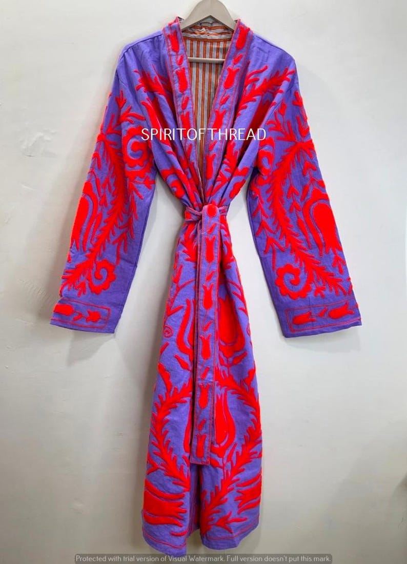 May include: A long, purple robe with vibrant red embroidered floral patterns. The robe features long sleeves and a matching tie belt. The text "SPIRIT OF THREAD" is visible on the front of the robe.