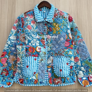 May include: A quilted jacket featuring a vibrant blue patchwork floral pattern, a light blue and white striped collar, and two front pockets with matching stripes and small red heart accents. The text "Spiritofthread" is printed in white.