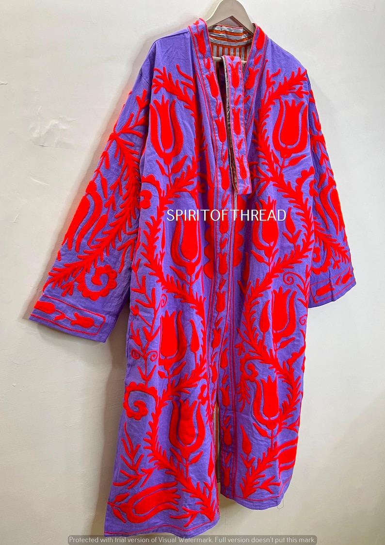 May include: A long, open-front robe in a vibrant purple hue, adorned with bold red floral embroidery. The robe features long sleeves and a detailed pattern, with the text "SPIRITOFTHREAD" visible. This garment is a striking piece of apparel.