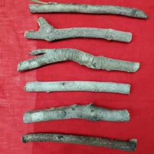 Peut inclure: Six branches de bois naturel de différentes longueurs et épaisseurs, disposées sur un fond de tissu rouge.