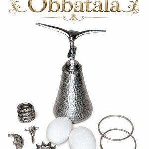 May include: A silver-toned metal bell with a hammered texture topped with a bird figure, accompanied by two white oval stones, two thin silver rings, a silver crescent moon, a silver sun, a silver cross, and a stack of silver rings. Text reads Herramientas de Obbatalá.