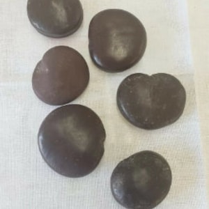 May include: Six dark brown, smooth, oval-shaped stones on a white fabric background.