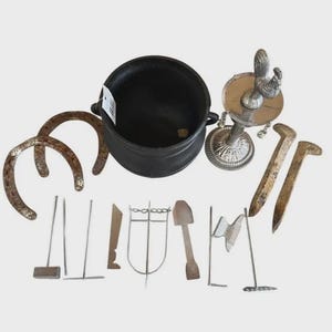 Peut inclure: Une collection d'objets comprenant un chaudron en fonte noire, deux fers à cheval en métal patiné, deux grands clous en métal, une lampe à huile en métal argenté avec un coq, et divers petits outils en métal comme des râteaux et des pelles.
