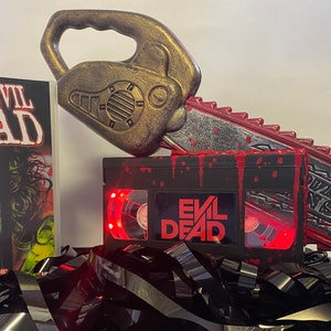 Lampada VHS Super Deluxe di Evil Dead con grande motosega e sangue. Un regalo horror per gli amanti dei film horror e gli appassionati di cinema.