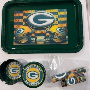 May include: Green Bay Packers themed smoking set with a green tray, two green and gold ashtrays, and two lighters with the team logo.