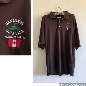 May include: Brown golf polo shirt with the Oaklands Golf Club logo and the text "Niagara Falls" embroidered on the left chest. The logo features a green golf course with a red flag and a white Canadian flag.