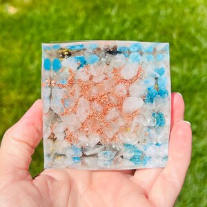 K&ouml;nnte beinhalten: Ein quadratisches Kristallgitter mit einer klaren Harzbasis. Das Gitter ist mit kleinen wei&szlig;en, blauen und kupferfarbenen Kristallen gef&uuml;llt.